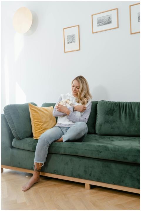 Blond woman sitting on green sofa, holding a cat i