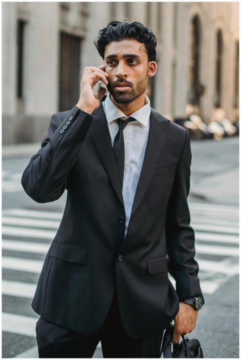 Confident businessman in black suit talks on a sma