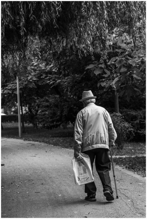 Elderly man in a hat walking on a park path with a