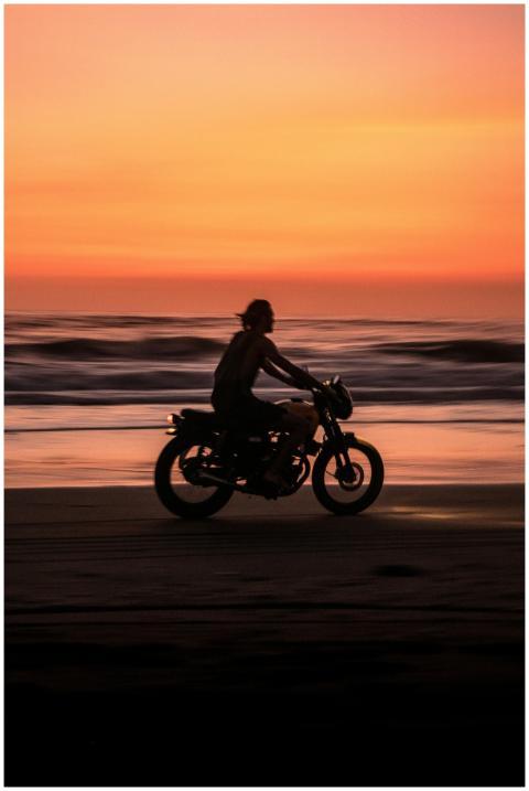 Silhouette of a motorcyclist riding on a beach in
