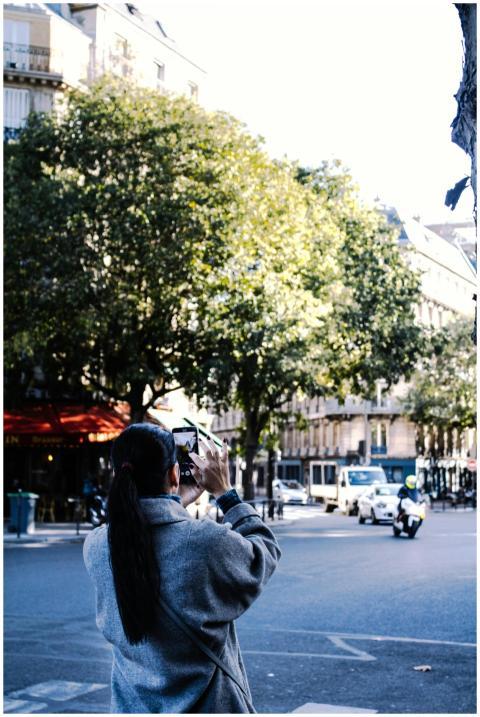 An adult woman photographs a bustling city street