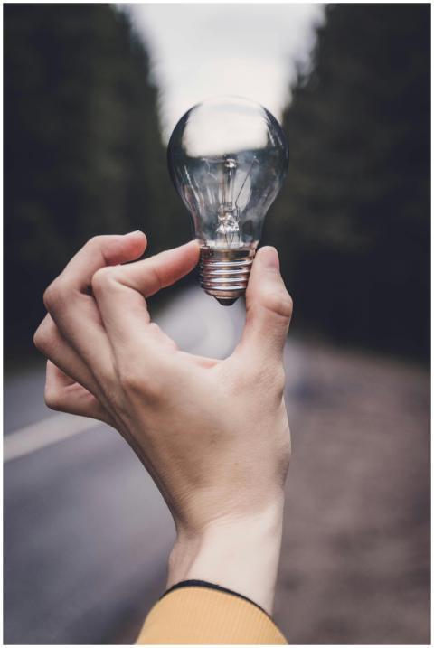 Close-up of a hand holding a lightbulb against a b