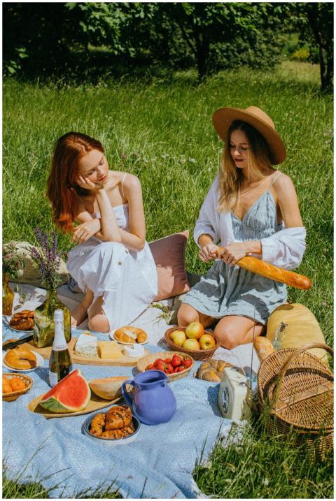 Two women enjoying a sunny picnic with fruits, bre