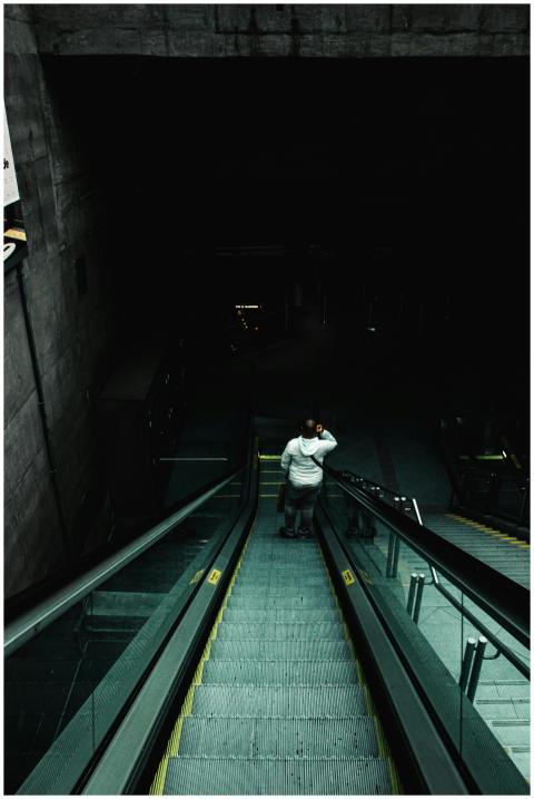 A lone figure descends a shadowy underground escal