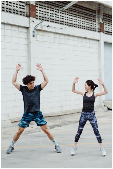 Energetic couple doing jumping jacks outdoors, sho