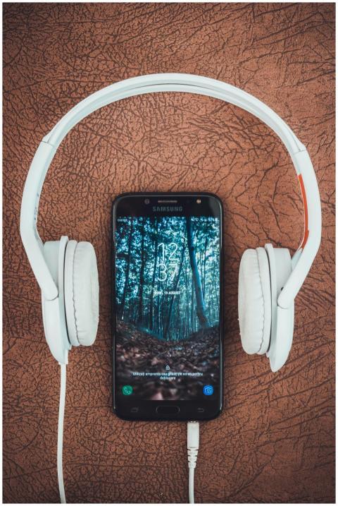 A smartphone paired with white headphones on a bro