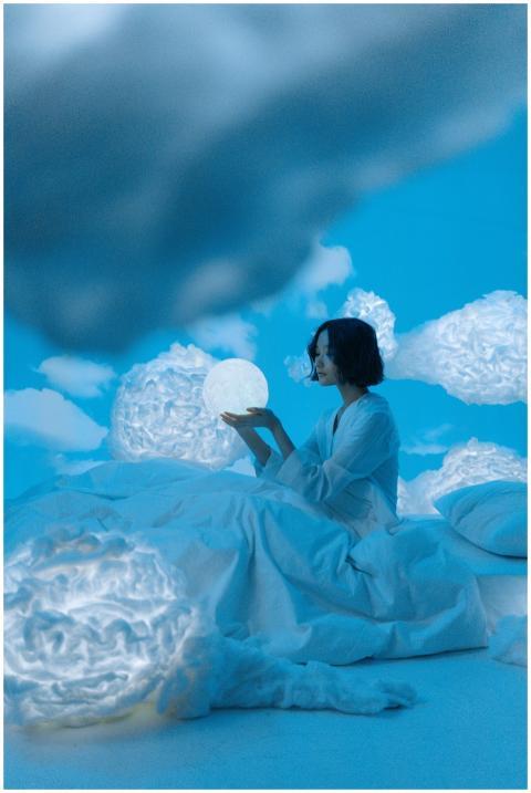 Asian woman holding glowing orb on bed in surreal