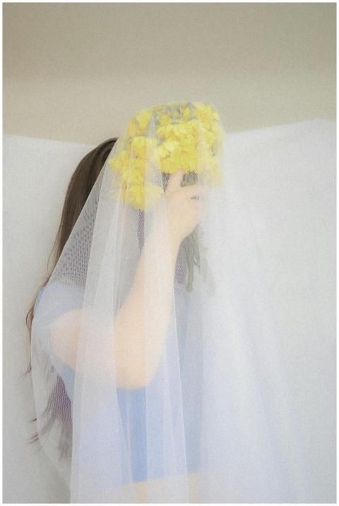 A woman holds yellow flowers under a delicate wedd