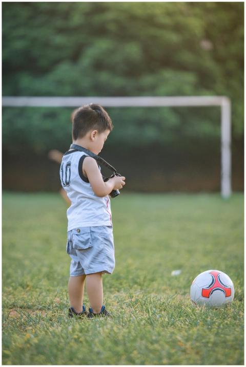 A young boy stands on a soccer field with a ball,