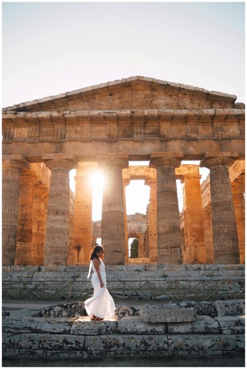A woman in a white dress walks by an ancient templ