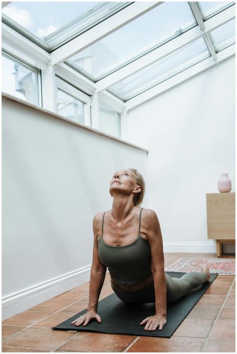 Elderly woman in yoga pose on mat in sunlit room,