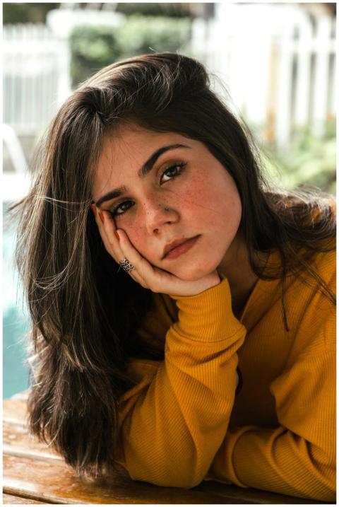 A young woman in a yellow sweater poses thoughtful