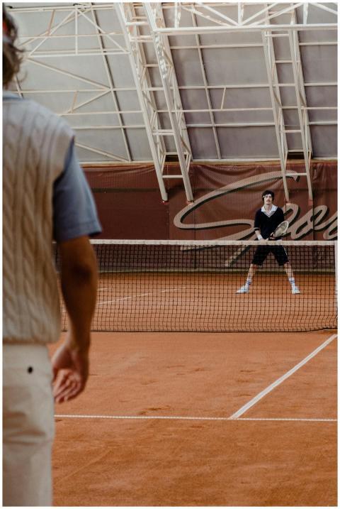 Two men playing tennis indoors on a clay court wit