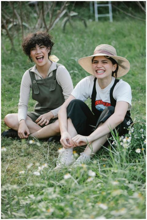 Two friends laughing together in a sunny meadow, e