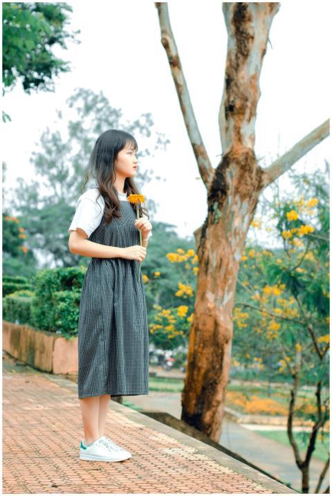 A young woman in a checkered dress holds a sunflow