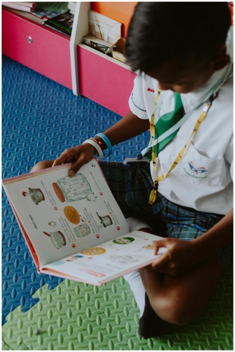 A child in school uniform reading a book on the fl