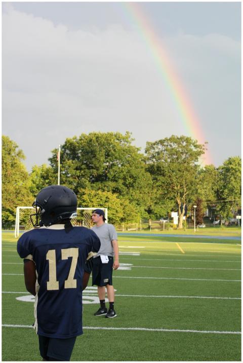 Football players and coach practice under a rainbo