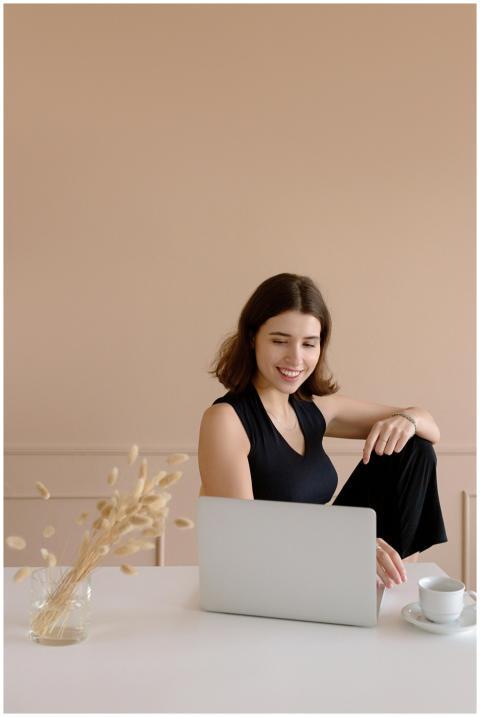 A cheerful woman works on her laptop at home, enjo