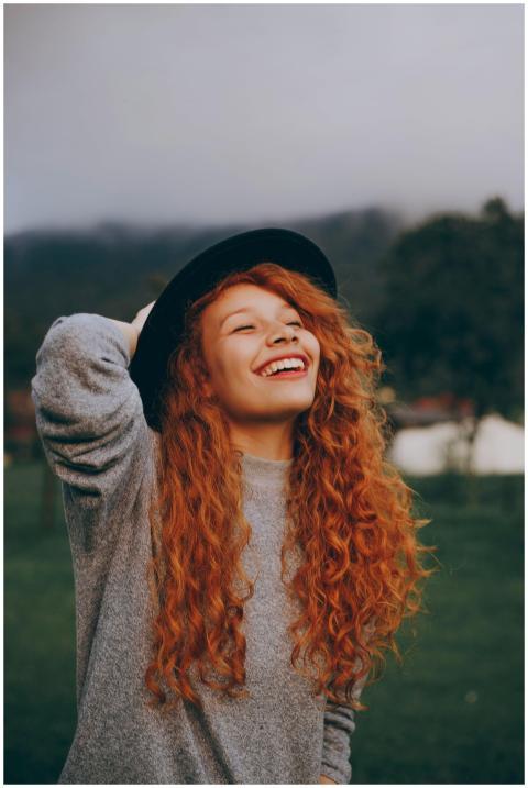 A happy young woman with curly red hair and a hat