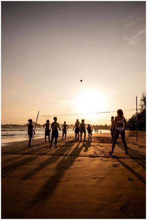 Silhouetted adults playing beach volleyball agains