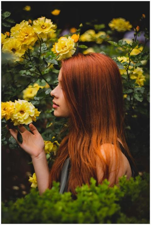 A woman with red hair enjoying the scent of bloomi