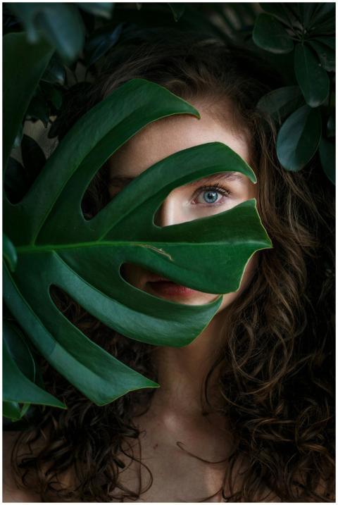 A beautiful woman peeks through lush green leaves