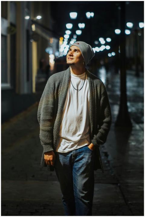 A young man walks through a dimly lit city street,