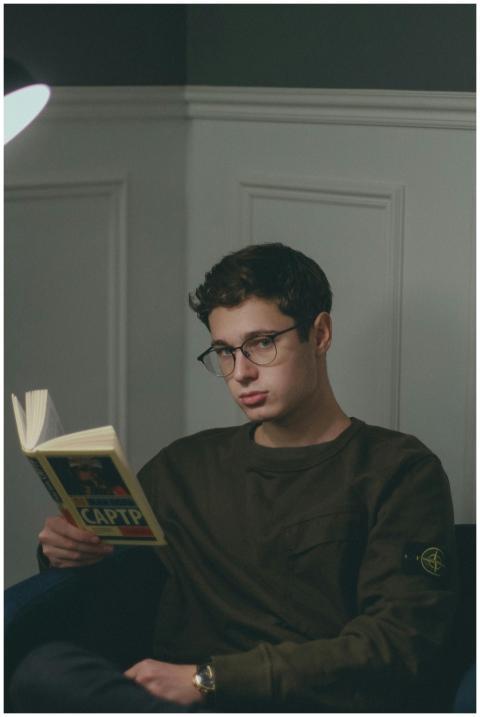 A young man wearing glasses reading a book in a co