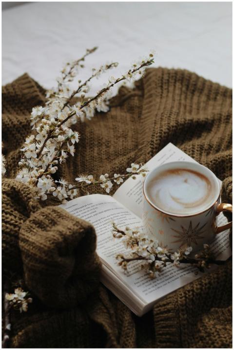Warm coffee and an open book on a knitted sweater,