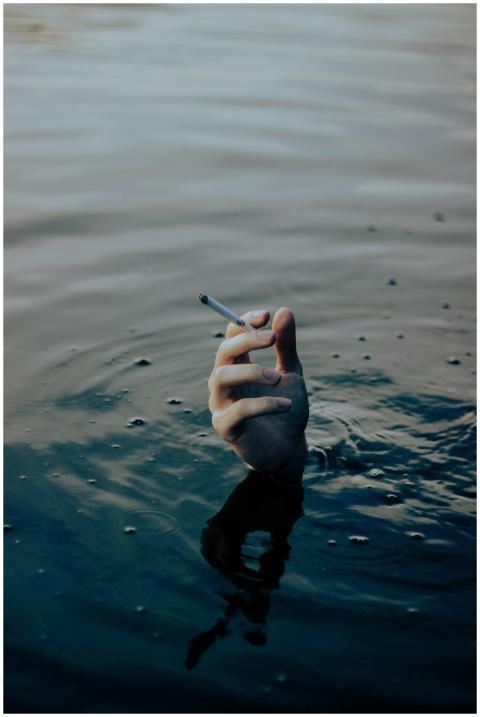 A hand emerging from water holds a cigarette, symb