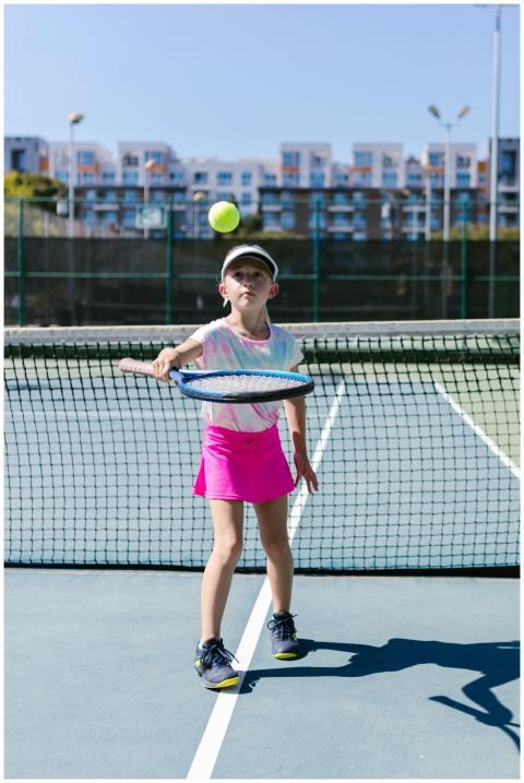 A young girl in pink sportswear playing tennis on