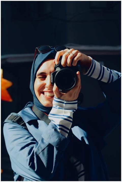 A cheerful female photographer in a hijab holding