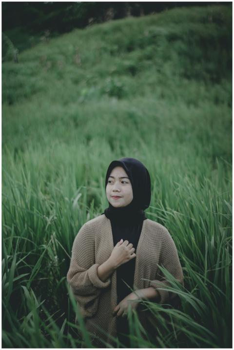 A woman in a hijab stands in a lush grassland in S