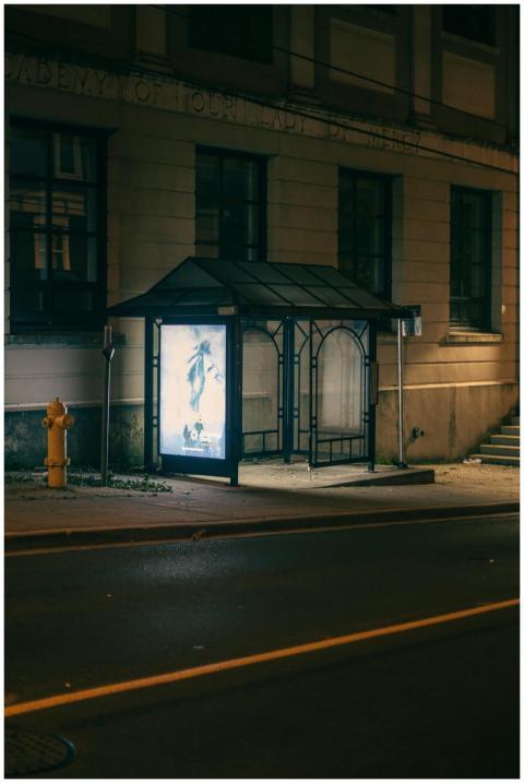An empty bus stop by a city sidewalk illuminated b
