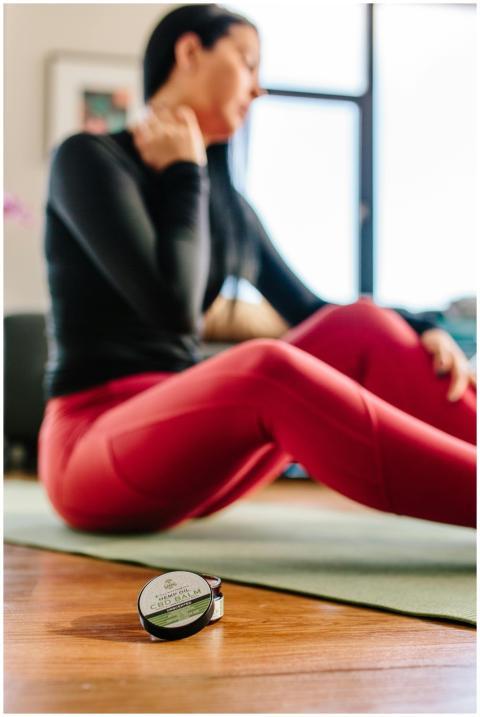 A woman sitting on a yoga mat indoors, using CBD c