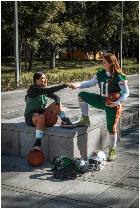 Two women in athletic gear share a fist bump, surr