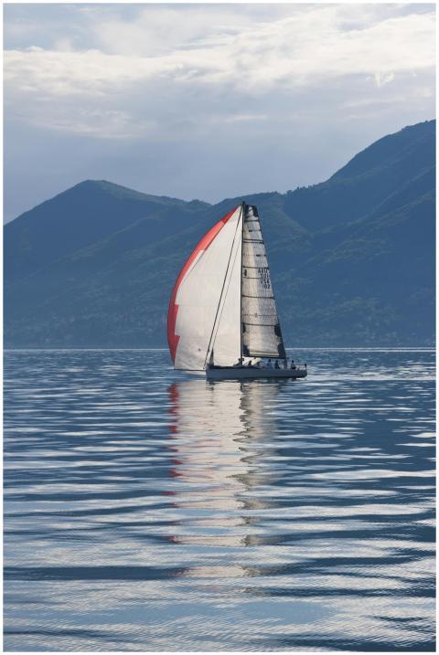 A sailboat glides through calm waters with mountai