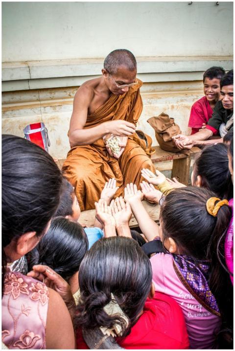 An Asian monk in orange robes distributes food to