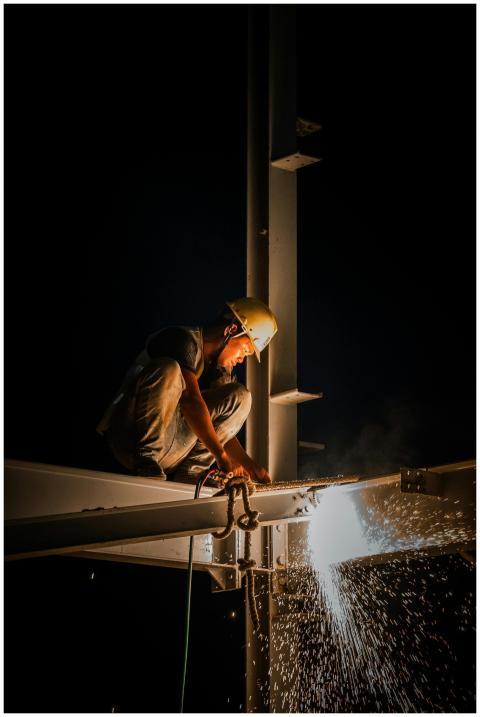 Industrial worker welding steel structure at night
