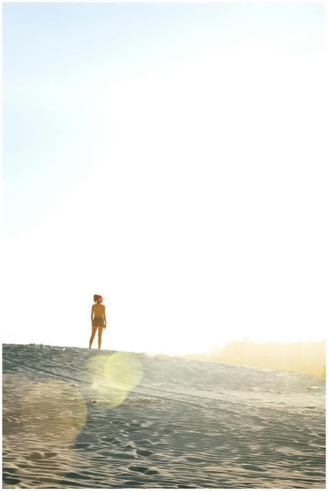 A person stands alone on a sandy beach under a bri