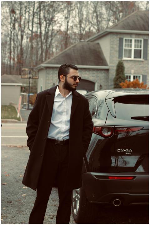 Fashionable man in coat and sunglasses beside car