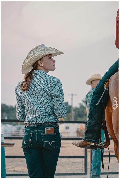 A young woman in a cowboy hat stands beside a hors