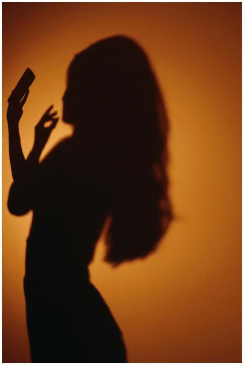 Silhouette of a woman holding a smartphone against