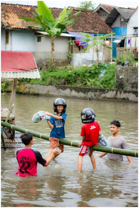 Children with helmets play on bamboo in a canal, e