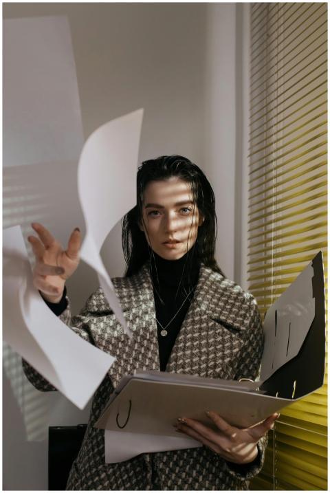 A businesswoman in a coat tosses papers in an offi