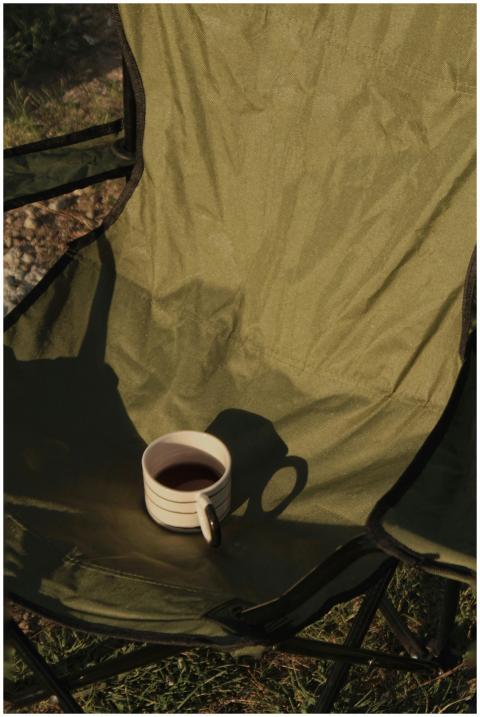 A cozy green camping chair holds a striped mug of