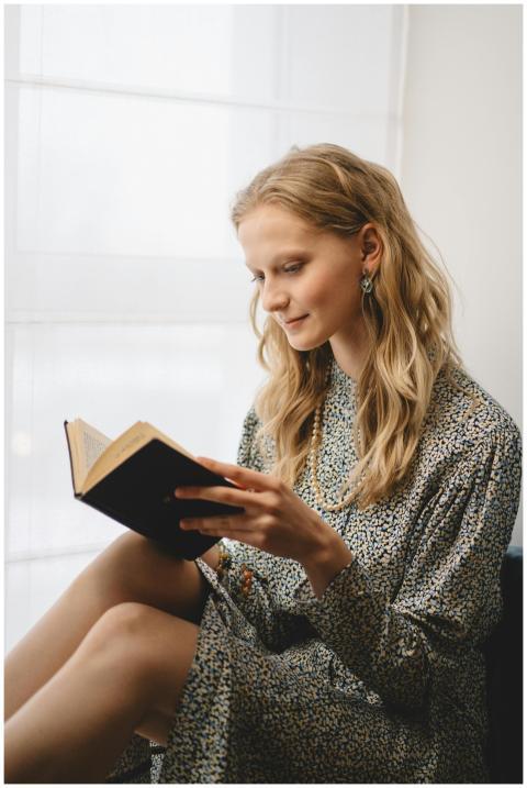A serene young woman enjoys a book by a sunlit win