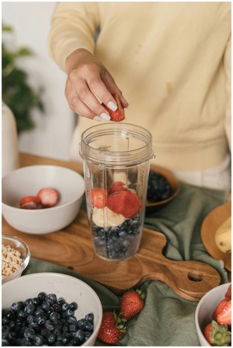 A person putting strawberries into a blender cup w