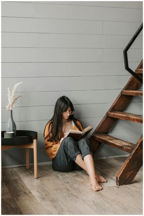 Young adult woman reading a book near wooden stair