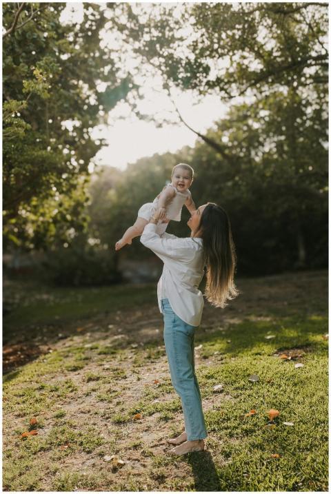 A mother joyfully lifts her baby in a sunny park s